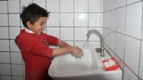 A young boy washes his hands with enthusiasm 