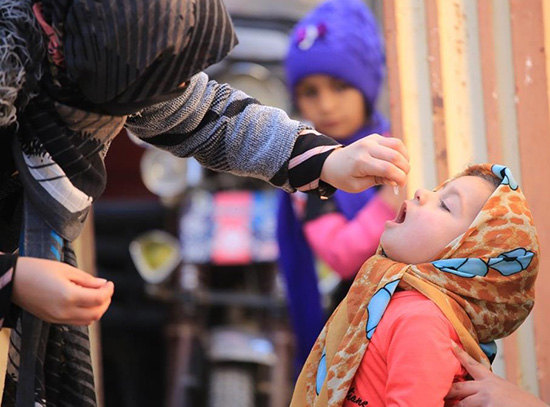 A toddler girl receives oral polio vaccine in recent campaigns in Afghanistan while an older girl looks on