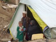 A woman and her two children sit outside their tent in an emergency camp