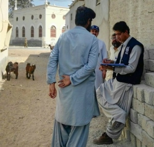 A WHO staff member interviews a man on a village street