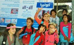 A_group_of_young_girls_pose_in_front_of_a_poster_providing_information_on_the_cholera_campaign