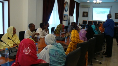 Un groupe d'hommes et de femmes djiboutiens sont assis autour d'une table et regardent sur un écran lumineux un texte commenté par un formateur debout à côté.