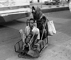 A man being pushed on a trolley by a woman while holding a baby.