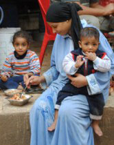 A photograph of a woman carrying a child while preparing food 