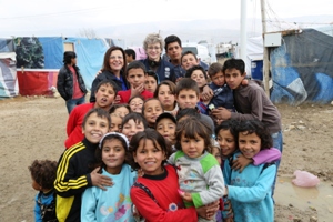 Displaced Syrian children posing with WHO staff in informal tented settlement