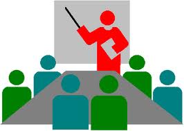 Dessin de type clipart représentant une session de formation : un formateur debout devant six personnes assises à une table pointe un tableau avec sa règle