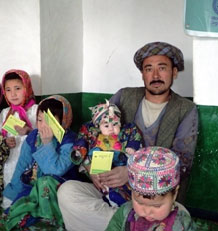 l’image nous montre un homme en Afghanistan assis avec ses quatre enfants qui montrent leur cartes de vaccination