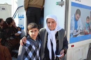 الجدة حياة ياسين مع ابنها بانتظار تلقي العلاج في عيادة طبية متنقلة. الصور: منظمة الصحة العالمية/"بولين أجيلو"