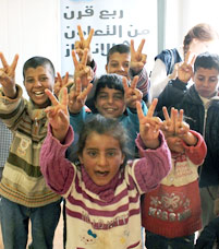 Des enfants syriens sourient en levant les bras pour faire le signe de la paix avec leurs doigts.