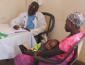 Assis à une table, un médecin africain rédige une ordonnance pour une patiente assise en face de lui, un jeune enfant sur ses genoux