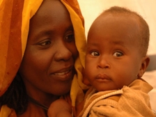 La photo nous montre une mère soudanaise qui sourit, son enfant dans les bras