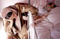 A tired Syrian mother comforts her son as he lies in his hospital bed breathing oxygen through a mask