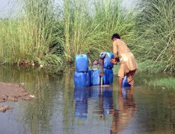 A man knee deep in flood water collects drinking water from a pump 