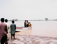 Following flash floods in Rajanpur, Punjab, Pakistan, three men go out in a small motor boat to conduct a rescue operation to save lives. Men watch them from the shore.