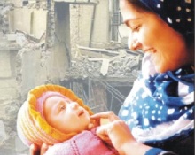 A photo of a mother holding her baby against the backdrop of an earthquake damaged building