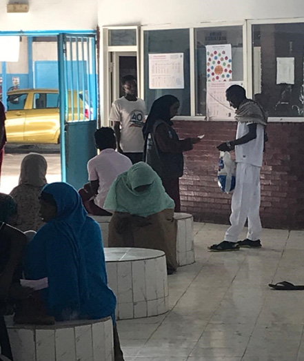A community health worker (standing, dressed in black) speaks to a study participant to discuss laboratory testing and to help him schedule his next appointment. Photo credit: WHO/A. Ali