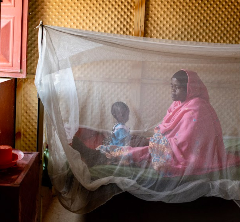 On 26 April 2022, a mother sits with her child under a mosquito net on a bed at a nutrition stabilization centre in Abu Shouk IDP camp in North Darfur. Photo credit: WHO/ Lindsay Mackenzie