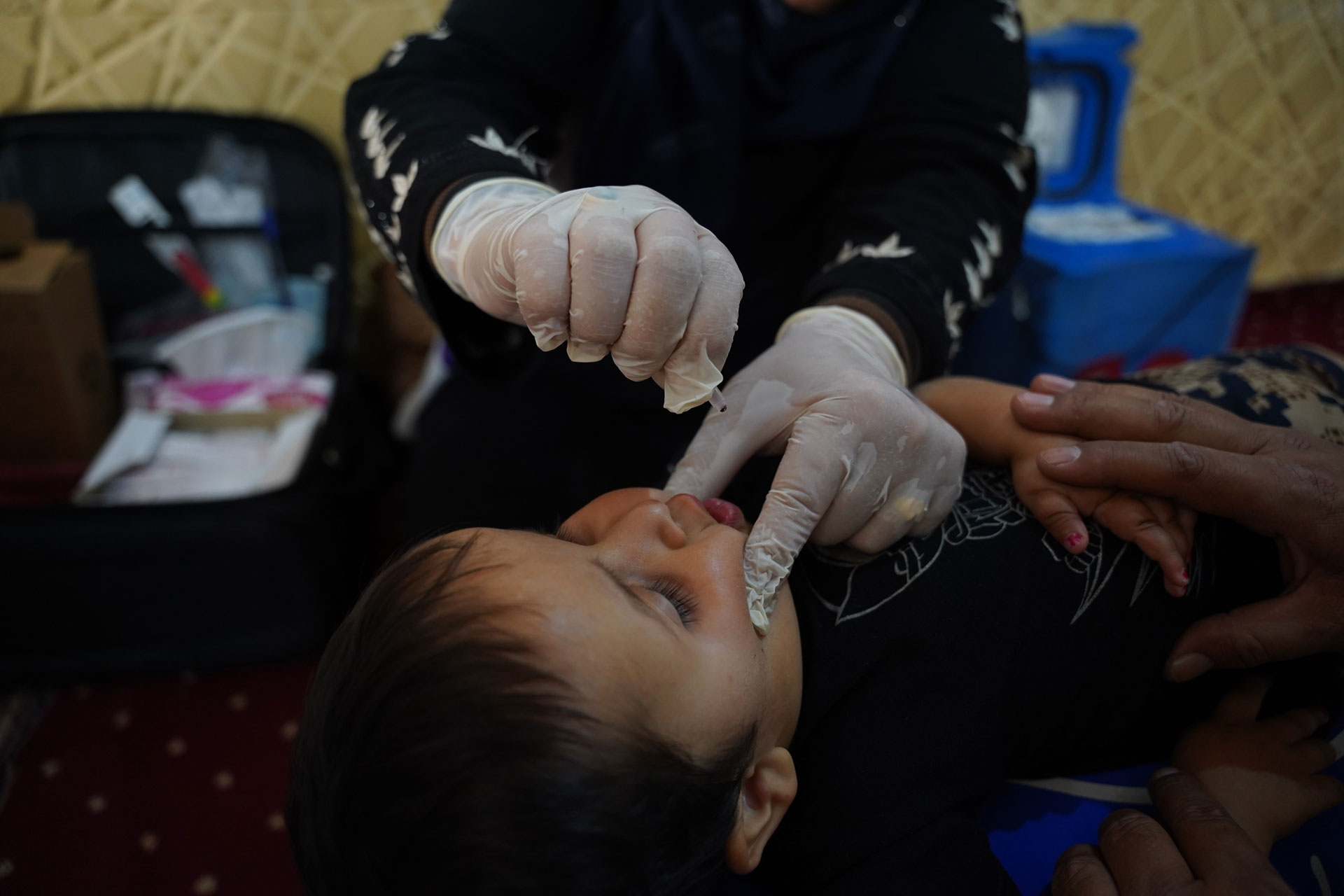 A health worker administers oral vaccine drops to Jameel’s child inside his family's temporary shelter. Photo: WHO