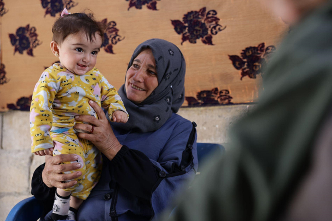 A mother holds her youngest child while waiting for routine vaccination in Khan Shaykhun. Photo: WHO A mother holds her youngest child while waiting for routine vaccination in Khan Shaykhun. Photo: WHO