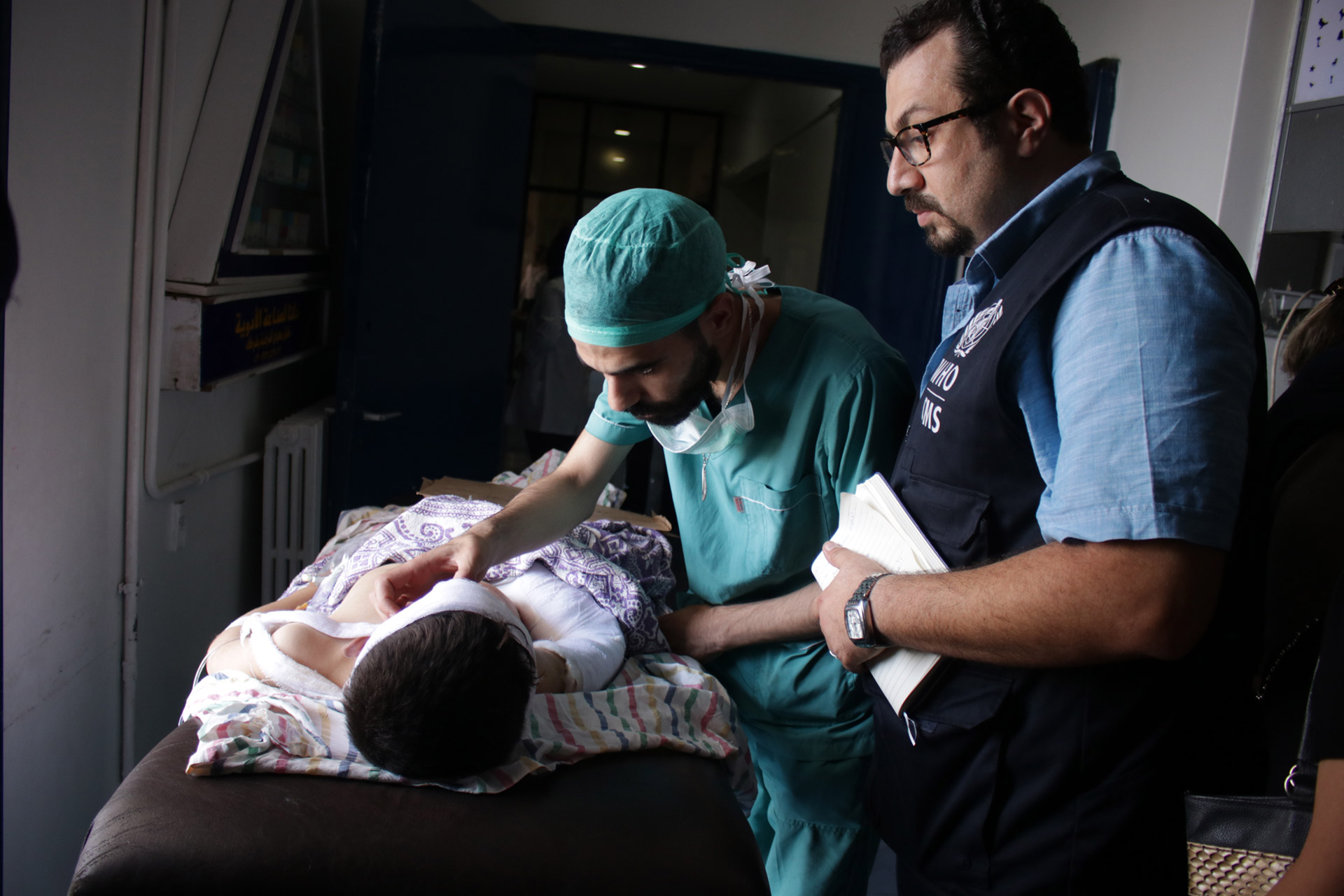 Dr Fares Kady speaks with a surgical resident at Aleppo University Hospital as he checks on a child injured by unexploded ordnance. Photo credit: WHO