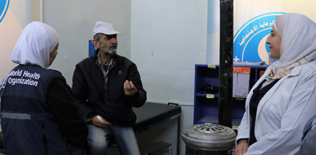 Kamal Qassis, 69, speaks with health workers during a follow-up visit at the Al-Birr Association health centre in Hama. Photo: WHO