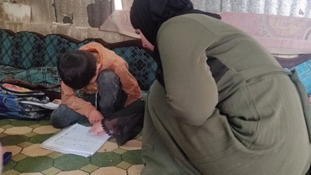Hana helps her youngest son with his homework at Sundian camp, Idlib governorate. Following the successful completion of her treatment, Hana has been able to re-engage in caring for her children. Photo credit: WHO/ Hope Revival Organization 