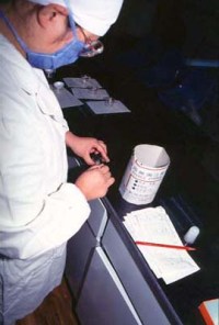 A technician making a smear slide, carrying out a test on a sputum sample to detect whether the person is infected with tuberculosis or not.
