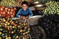 Un petit garçon souriant est assis dans un marché au milieu de caisses de fruits et de légumes