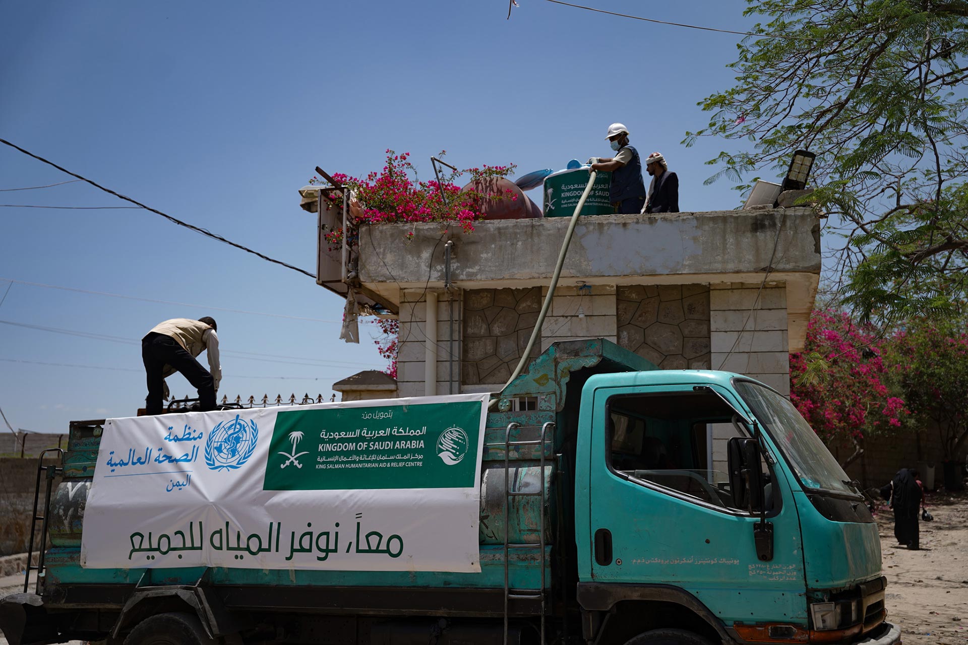 Workers fill a rooftop water tank from a truck bearing WHO and Kingdom of Saudi Arabia aid banners, part of a water supply initiative in Yemen