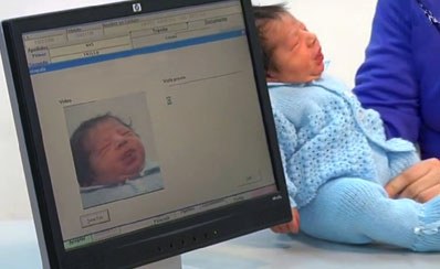 A baby is held next to a computer screen and the baby's image is recorded on the screen