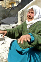 A picture of a veiled older woman in anguish sitting near the steps of a ruined property