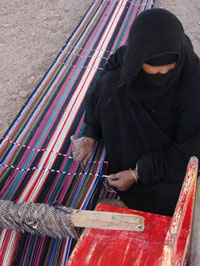 Jordanian woman in traditional dress weaving a carpet