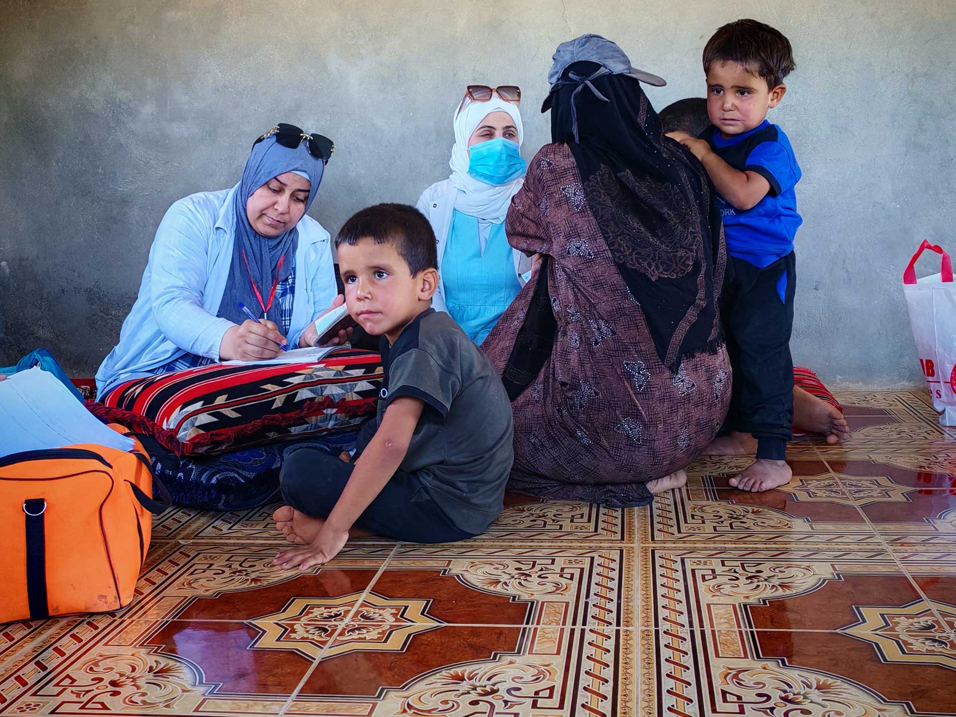 Children sit beside their mother as she receives care from a WHO-supported Al Bir mobile team in rural Hama. The teams deliver primary health services directly to people’s homes, ensuring no one is left behind.   Photo credit: WHO 