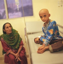 An image of a child without any hair sitting on a hospital bed with the mother looking on