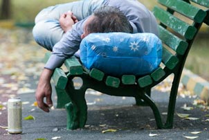 La photo nous montre un homme allongé sur un banc de parc