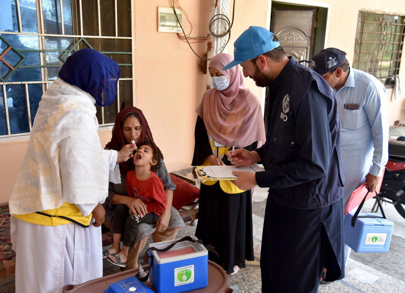 Health workers administer oral polio vaccine to a child during a door-to-door immunization campaign, supported by WHO.