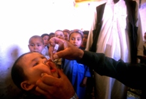 A young child receiving a polio vaccine during a national immunization day in Pakistan. Behind him is a line of children waiting to receive their vaccinations.
