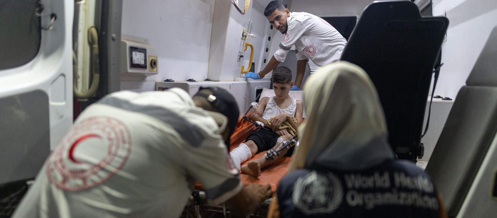 Medical teams provide urgent care to an injured child inside an ambulance, with support from the World Health Organization and the Palestine Red Crescent Society