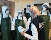 A trainer gives instructions to health workers wearing protective masks, goggles, gloves, hoods and coveralls 