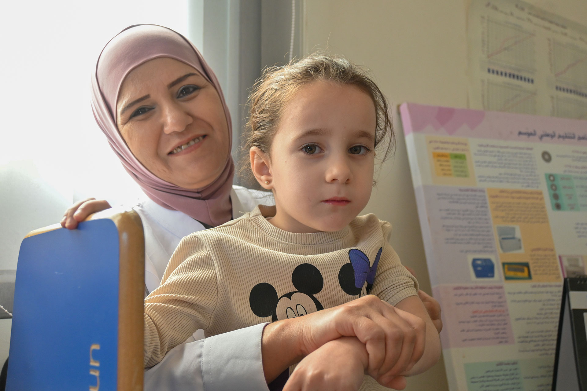 A vaccination officer in Damascus, holds seven-year-old Lyn Saleh Al-Akklah after checking her vaccination status  at Barzeh Al-Balad Health Centre. Photo credit: WHO