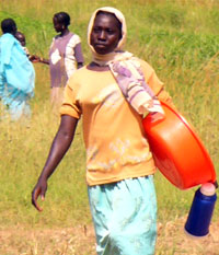 A young girl carrying a plastic bowl and a flask out of the fields